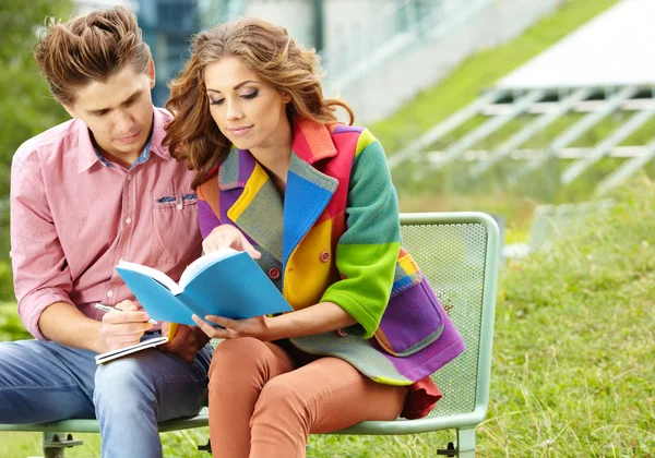 Casal de alunos com sentado no parque do campus e livro de leitura — Fotografia de Stock