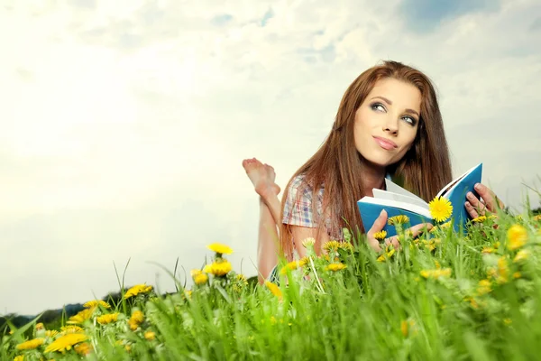 Mooi meisje ligt op weide en leest de boo — Stockfoto