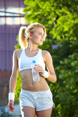 Açık havada su içen neşeli genç ve çekici bir kadın.