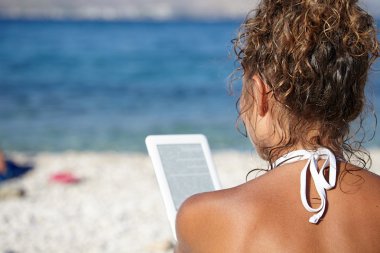 kadın tatilde kitap okuyarak sahilde bir e-okuyucu ile.