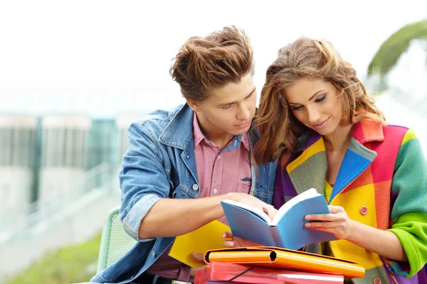 Couple of students sitting outdoors studying and smiling — Stock Photo, Image