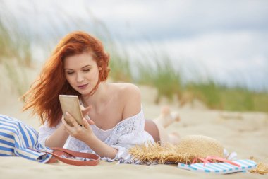 Güzel genç kadın bir smartphone, sahilde yalan kullanır