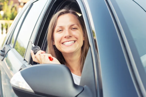 Jovem senhora sentada em um carro e mostrando a chave — Fotografia de Stock