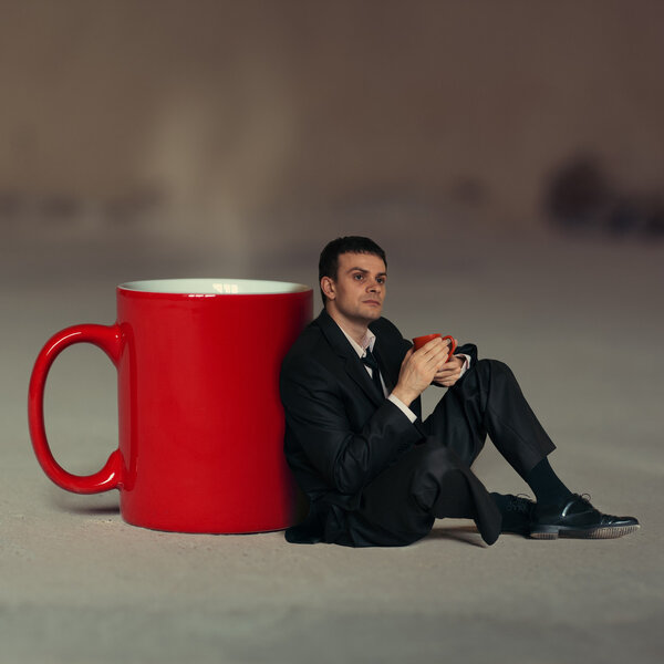 Businessman with a cup of tea sitting around a large cup