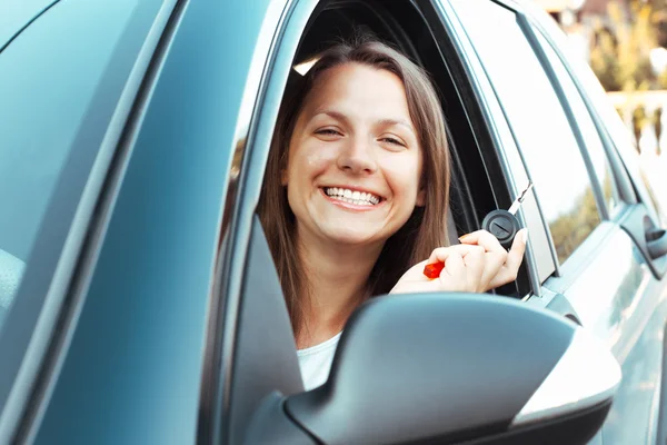 Sonriente chica sentada en un coche y mostrando la llave —  Fotos de Stock