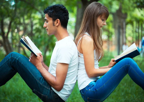 Студенты спина к спине читают книгу на открытом воздухе — стоковое фото