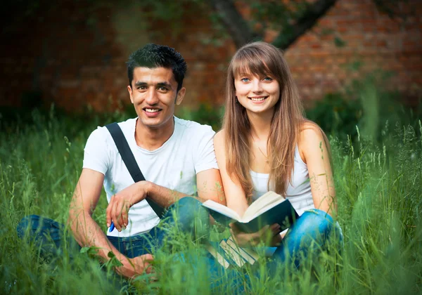 Doi studenți tip și fată care studiază în parc pe iarbă cu carte — Fotografie, imagine de stoc