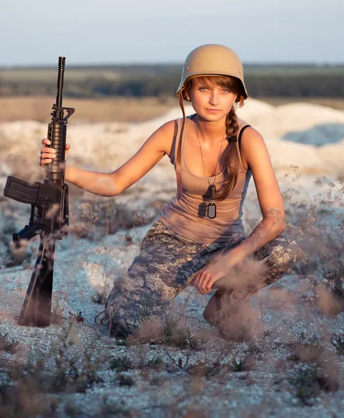 Ung kvinnlig soldat klädd i ett kamouflage med en pistol i o — Stockfoto