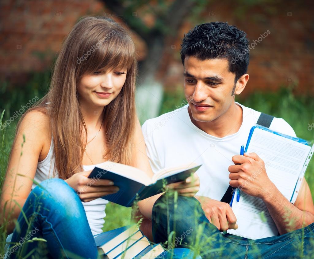Two students studying in park on grass with book outdoors