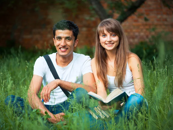Два студента в парке на траве с книгой на открытом воздухе — стоковое фото