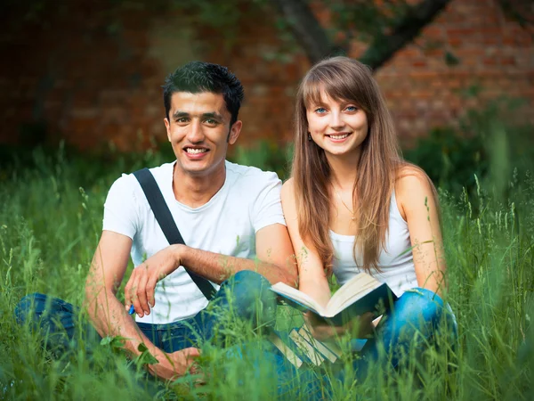 Två studenter i parken på gräs med bok utomhus — Stockfoto