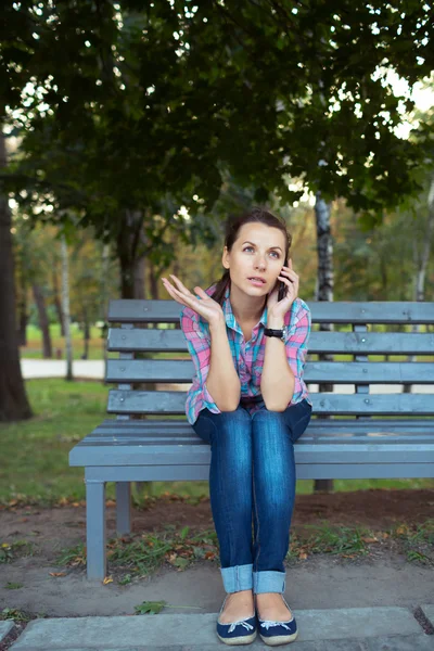 Πορτραίτο μιας γυναίκας σε ένα πάρκο σ ' ένα παγκάκι, μιλώντας στο τηλέφωνο — Φωτογραφία Αρχείου