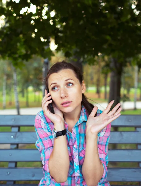 Portrait of a young woman in a park talking on the phone — Stock Photo, Image