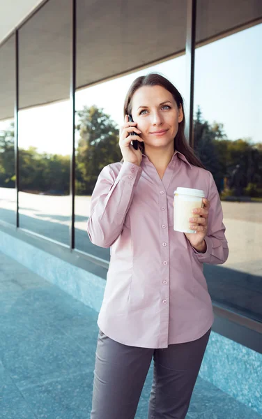 Femme d'affaires avec téléphone portable et café tout en se tenant contre o — Photo