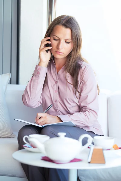 Businesswoman talking on the phone and writing in organizer in a — Stock Photo, Image