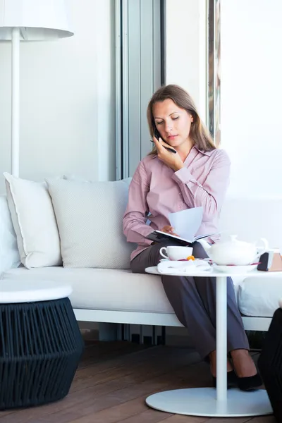 Businesswoman talking on the phone and writing in organizer in a — Stock Photo, Image