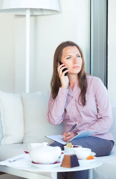 Businesswoman talking on the phone and writing in organizer in a — Stock Photo, Image