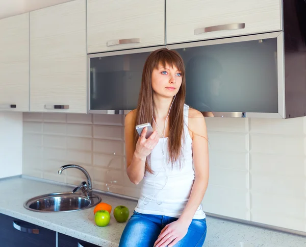 Молодая девушка на кухне слушает музыку в наушниках — стоковое фото