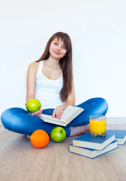 Mladá brunetka s apple čtení knihy doma — Stock fotografie
