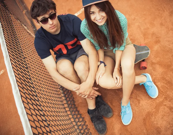 Couple sitting on a skateboard on the tennis court — Stock Photo, Image