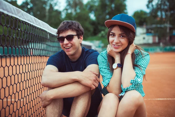 Junges Paar sitzt auf einem Skateboard auf dem Tennisplatz — Stockfoto