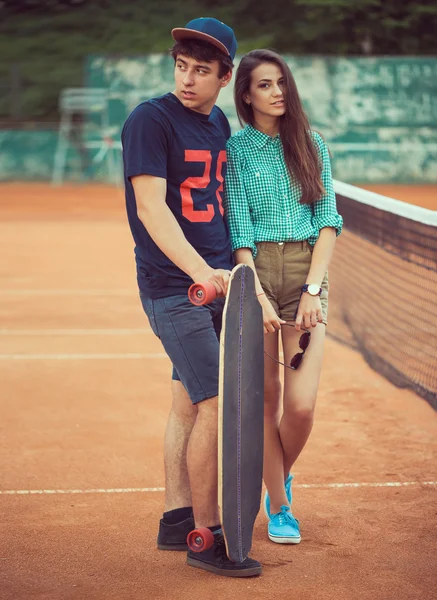 Jong koppel staande op een skateboard op de tennisbaan — Stockfoto