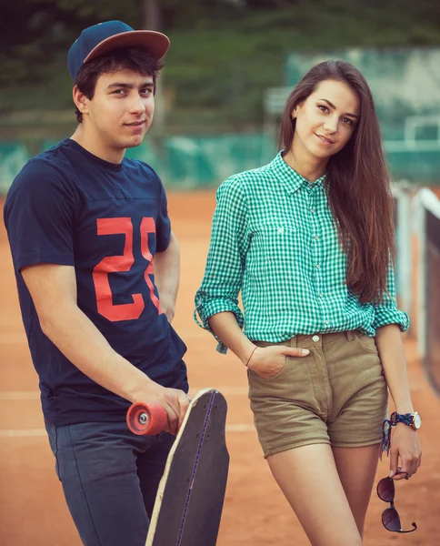 Junges Paar steht auf einem Skateboard auf dem Tennisplatz — Stockfoto