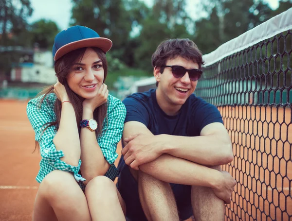 Jovem casal sentado em um skate na quadra de tênis — Fotografia de Stock