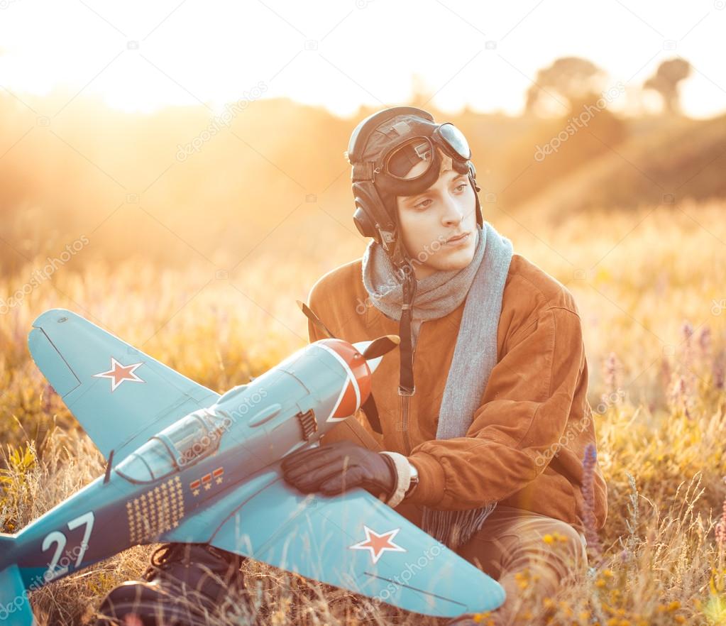 Guy in vintage clothes pilot with an airplane model outdoors