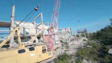FPV insansız hava aracı, terk edilmiş sanayi binaları ve bir kazıcının etrafında hızla ve manevra kabiliyetiyle uçar..