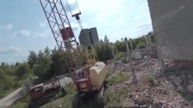 FPV insansız hava aracı, terk edilmiş sanayi binaları ve bir kazıcının etrafında hızla ve manevra kabiliyetiyle uçar..