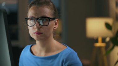 Gözlüklü kadın monitöre bakıyor ve internette sörf yapıyor. Monitör ekranı gözlüklere yansıyor. Gece çalış. İçişleri Bakanlığı. Uzak çalışma