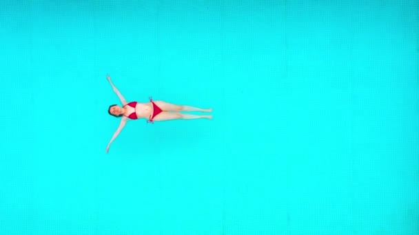 从上往下看，就像一个穿着红色泳衣的女人躺在游泳池里。放松的概念 — 图库视频影像