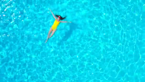 Blick von oben auf eine Frau in einem gelben Badeanzug, die auf dem Rücken im Pool liegt. Entspanntes Konzept — Stockvideo