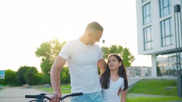 Pappa och dotter går runt i sitt område efter att ha cyklat i solnedgången. Långsamma rörelser — Stockvideo