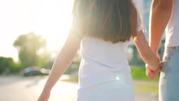 Papà e figlia camminano intorno alla loro zona al tramonto. Il bambino tiene per mano i padri. Vista posteriore. — Video Stock