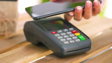 Akıllı telefondan yapılan temassız ödeme. Kablosuz ödeme konsepti. Yakın plan, kadın banka terminalindeki siparişi ödemek için akıllı telefon nakitsiz cüzdan teknolojisi kullanıyor..