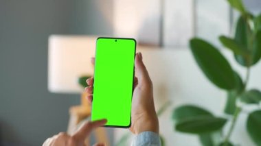 Evde dikey modda yeşil ekranlı akıllı telefon kullanan bir kadın var. Kız internette geziniyor, içeriği izliyor, videolar izliyor. POV.