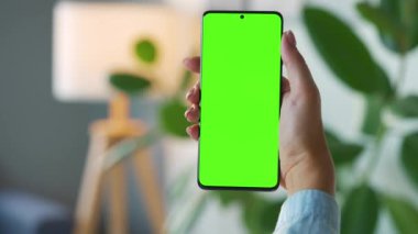 Evde dikey modda yeşil ekranlı akıllı telefon kullanan bir kadın var. Kız internette geziniyor, içeriği izliyor, videolar izliyor. POV.