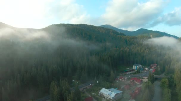 Vlucht over een bergresort tussen het naaldbos. Mist stijgt over de berghellingen — Stockvideo