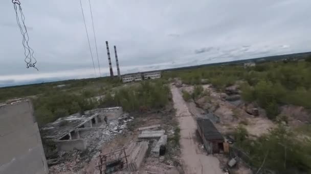 El dron FPV vuela rápido y maniobrable entre edificios industriales abandonados y alrededor de una excavadora. — Vídeo de stock