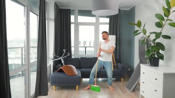 Hombre limpiando la casa y divirtiéndose bailando y cantando con una escoba — Vídeo de stock