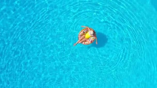 Vista aérea de uma mulher de fato de banho amarelo deitada num donut na piscina — Vídeo de Stock