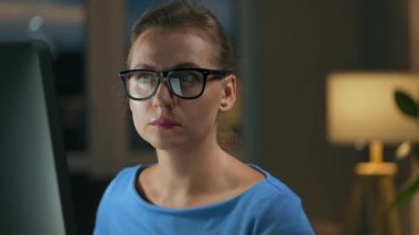 Gözlüklü kadın monitöre bakıyor ve internette sörf yapıyor. Monitör ekranı gözlüklere yansıyor. Gece çalış. İçişleri Bakanlığı. Uzak çalışma