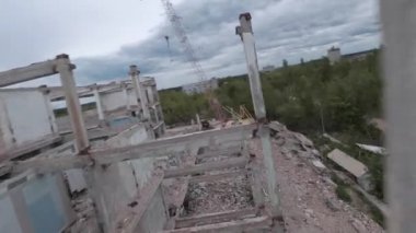 FPV insansız hava aracı, terk edilmiş sanayi binaları ve bir kazıcının etrafında hızla ve manevra kabiliyetiyle uçar..