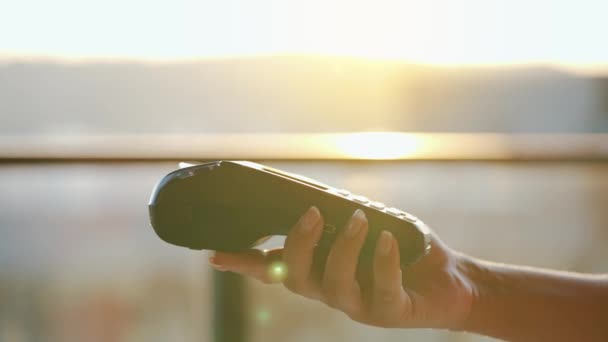 Κοντινό πλάνο, ο άνθρωπος που χρησιμοποιεί το smartphone χωρίς μετρητά τεχνολογία πορτοφόλι NFC για να πληρώσει την παραγγελία στο τερματικό τράπεζα. Μηχανή χαρτιών στο γυναικείο χέρι στο φόντο του ηλιακού φωτός — Αρχείο Βίντεο