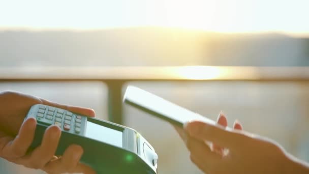 クローズアップ、女性は銀行ターミナルで注文を支払うためにスマートフォンのキャッシュレス財布NFC技術を使用しています。太陽の光を背景に男性の手でカードマシン — ストック動画