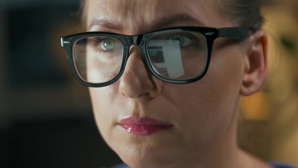 戴眼镜的女人看着监视器和上网。显示器屏幕反映在眼镜上.晚上工作。内政部。远程工作 — 图库视频影像