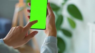 Evde dikey modda yeşil ekranlı akıllı telefon kullanan bir kadın var. Kız internette geziniyor, içeriği izliyor, videolar izliyor. POV.