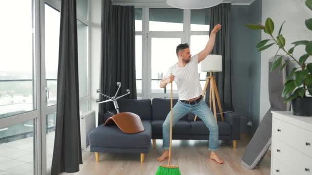 Hombre limpiando la casa y divirtiéndose bailando con una escoba. Movimiento lento — Vídeo de stock